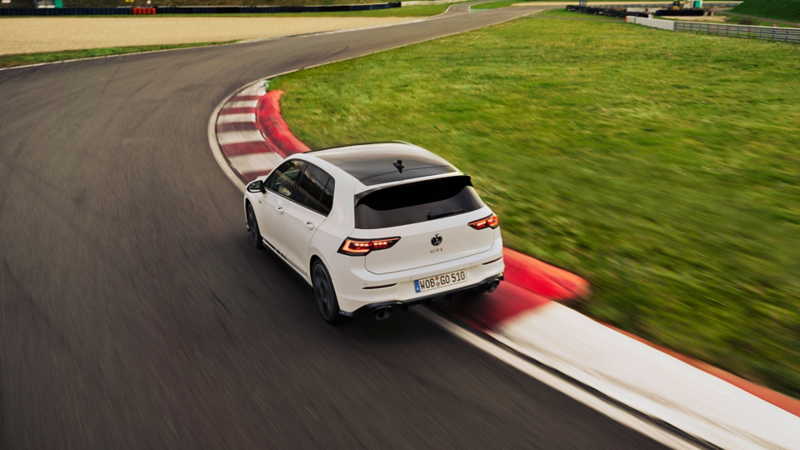 Vista posteriore di una VW Golf GTI Clubsport bianca che affronta una curva su un circuito.