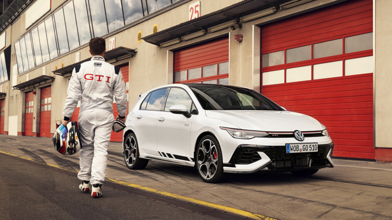 Un pilote s'approche de la Golf GTI Clubsport stationnée dans es stand d'un circuit.