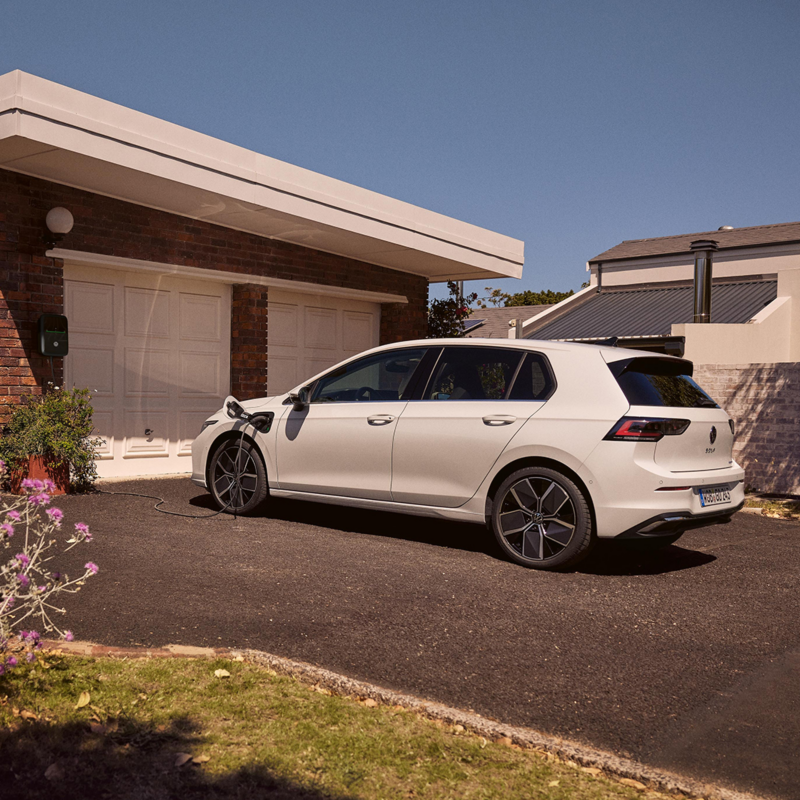 Vue arrière d'une Golf eHybrid devant l'entrée de son garage, branchée à une borne murale.