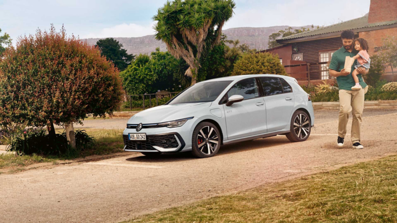 Ein Mann mit einem Mädchen auf dem Arm geht an einem weißen VW Golf GTE vorbei.