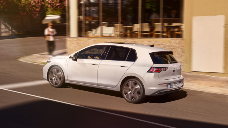 Ein weißer VW Golf fährt an einem Café vorbei.