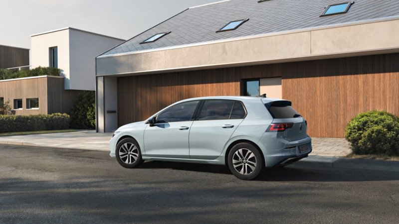 Ein  VW Golf ENERGY parkt vor einem Haus mit Holzfasse auf einem Stellplatz.