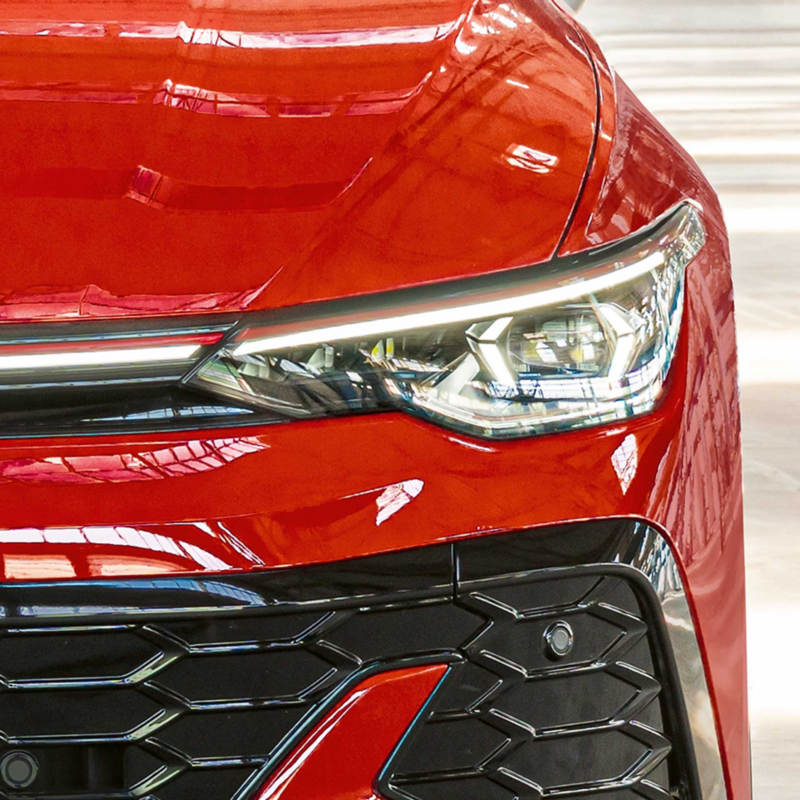 Close‑up of a red Volkswagen Golf GTI 50 Editions front headlight and grille inside a factory hall.