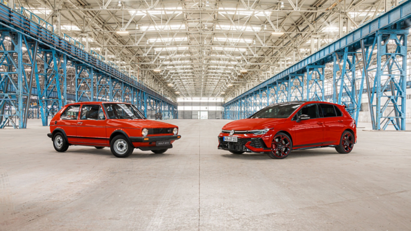 An old red VW Golf GTI and the new Golf GTI EDITION 50 in red are shown facing each other inside a factory hall.