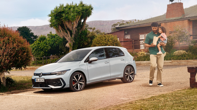 Mann mit Kind auf dem Arm geht zu einer Picknickbank, daneben parkt ein VW Golf GTE.