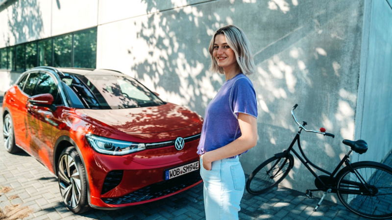 Kobieta stoi przed czerwonym elektrycznym  samochodem marki Volkswagen