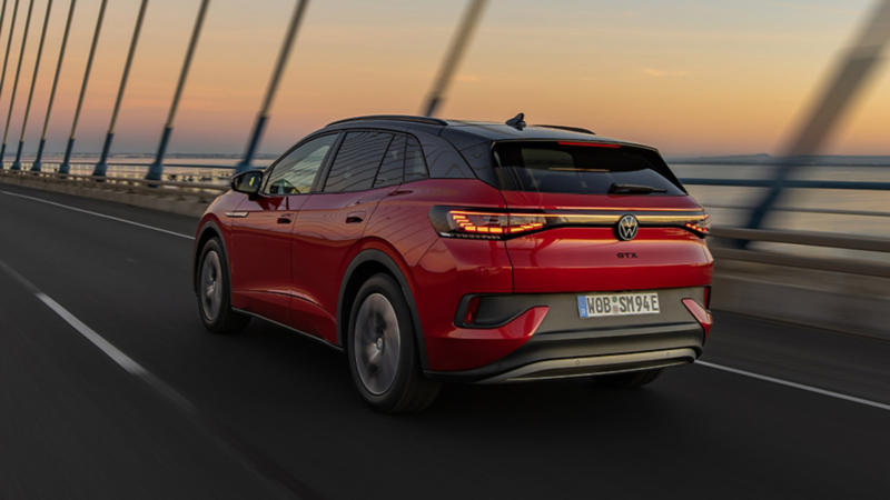Ein roter VW ID.4 GTX fährt bei Dämmerung über eine Brücke.
