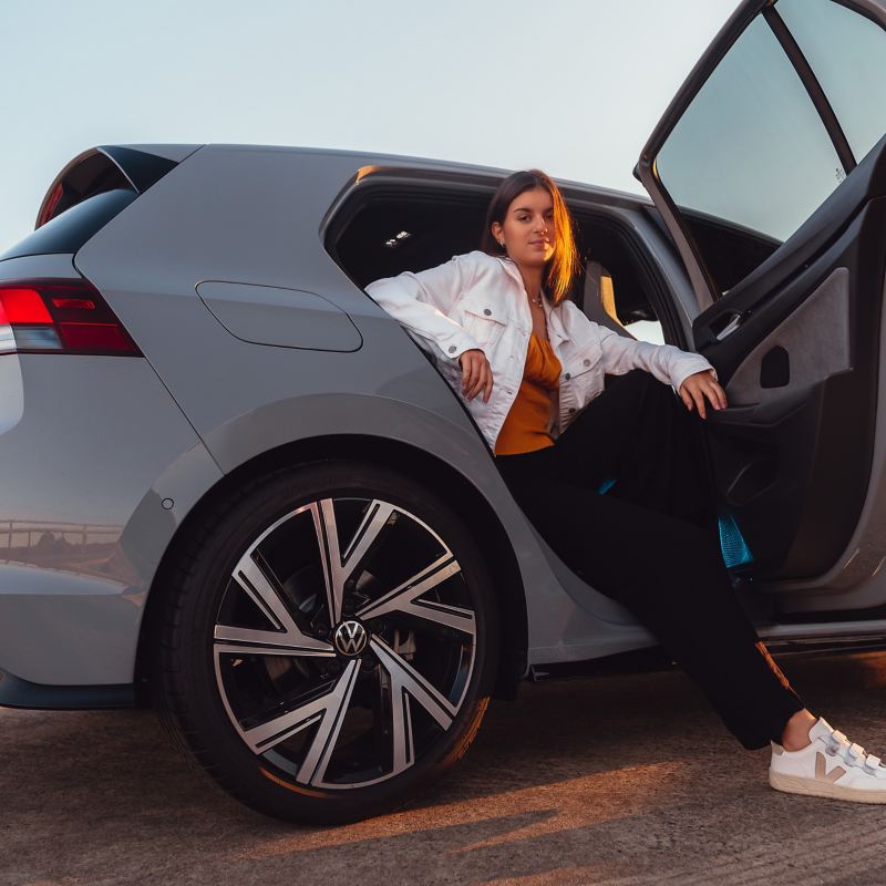 Woman walking past mera in foreground with rear view of Volkswagen Golf in background.
