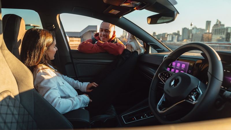 High angle view of pomelo yellow Volkswagen Golf with woman standing through sunroof of car and man jumping next to open door.
