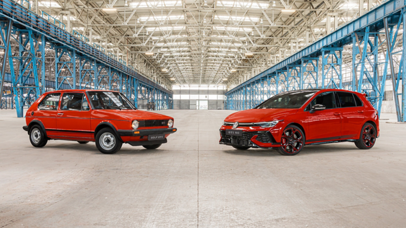 An old red VW Golf GTI and the new Golf GTI EDITION 50 in red are shown facing each other inside a factory hall.