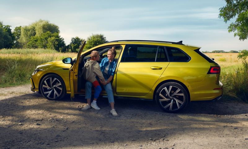 VW Golf Variant in Gelb von der Seite mit offener Fahrertür. Frau sitzt auf dem Fahrersitz mit Kind auf dem Schoß.