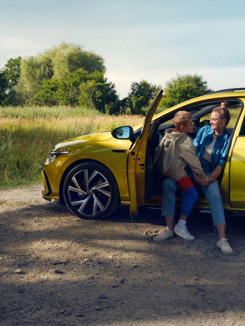 VW Golf Variant in Gelb von der Seite mit offener Fahrertür. Frau sitzt auf dem Fahrersitz mit Kind auf dem Schoß.
