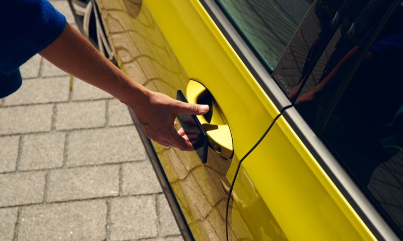 A woman uses her smartphone as a mobile key to open the door of a VW Golf.