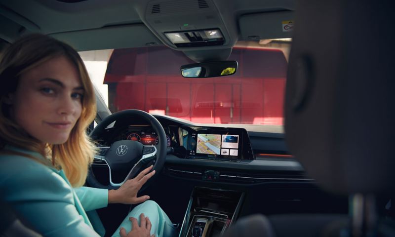 Une femme est assise côté conducteur dans une Golf avec le système d'infodivertissement allumé