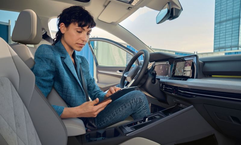 Blick vom Beifahrersitz auf eine Frau auf dem Fahrersitz im VW Golf, helles Interieur. Sie nutzt den integrierten WLAN-Hotspot über ein Tablet.