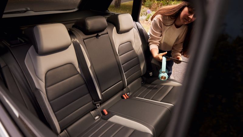 View of the rear bench seat in the VW Golf Estate. A woman leans into the car with the door open, holding a headset and a tablet.