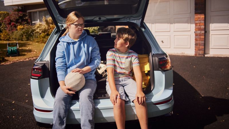 Ein Junge und ein Mädchen sitzen im Kofferraum eines weissen VW Golf Estate.
