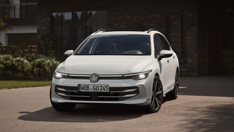 En vit VW Golf sportscombi är parkerad på uppfarten, strålkastarna fram är lyser