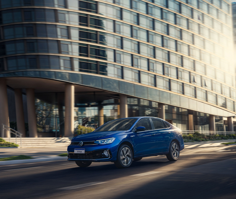 Volkswagen Virtus azul 2024 en movimiento frente a un edificio moderno, destacando su diseño elegante y características avanzadas.
