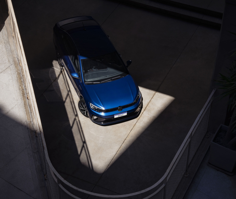 Vista aérea de un Volkswagen Virtus 2024 azul estacionado en un área iluminada, destacando su diseño moderno y elegancia.