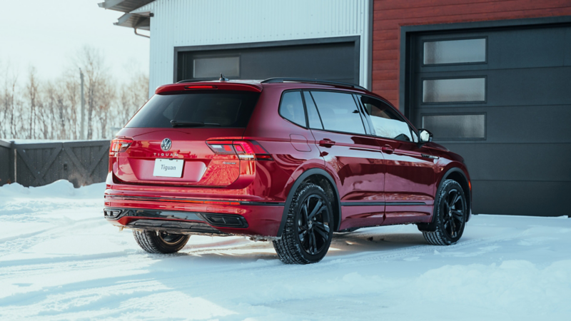 Vue arrière d'un Volkswagen Tiguan rouge garé dans une allée enneigée à côté d'une maison moderne.