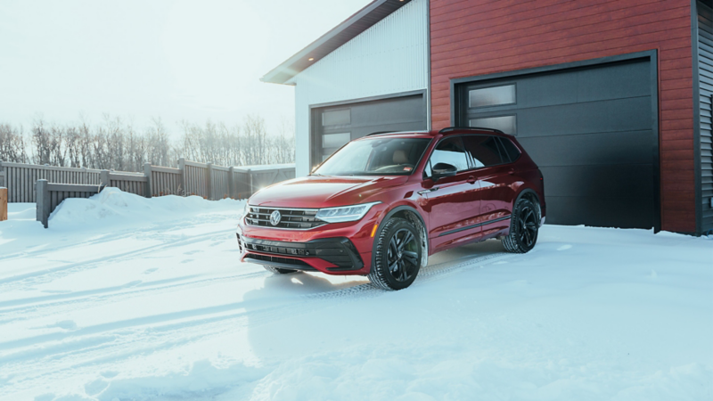 Vue de face d'un Volkswagen Tiguan rouge garé dans une allée enneigée.