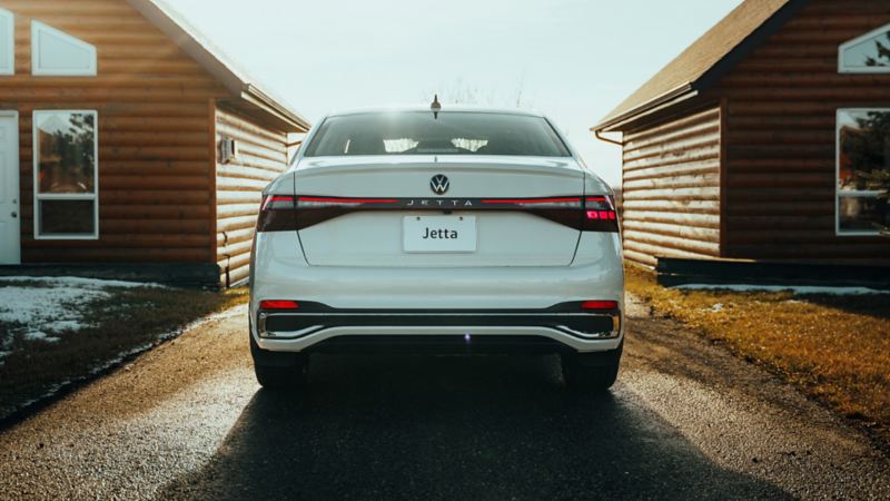 Vue arrière d'une Volkswagen Jetta blanche garée devant un chalet en bois rond.