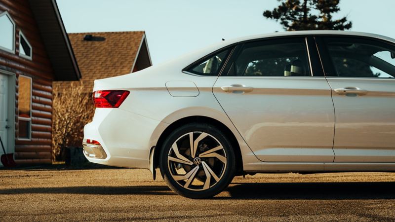 Vue de côté d'une Volkswagen Jetta blanche garée devant un chalet en bois rond.