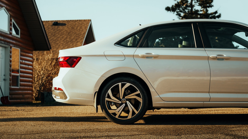 Rear view of a white Volkswagen Jetta parked in front of a log cabin.