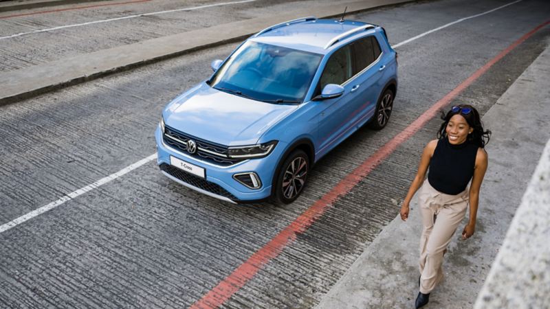 Man and woman standing by a flower stand, behind them a blue VW T-Cross in front of a mountainous landscape.