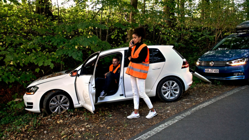 Woman with safety vest and Volkswagen Roadside Assistance employee next to VW ID. with open bonnet