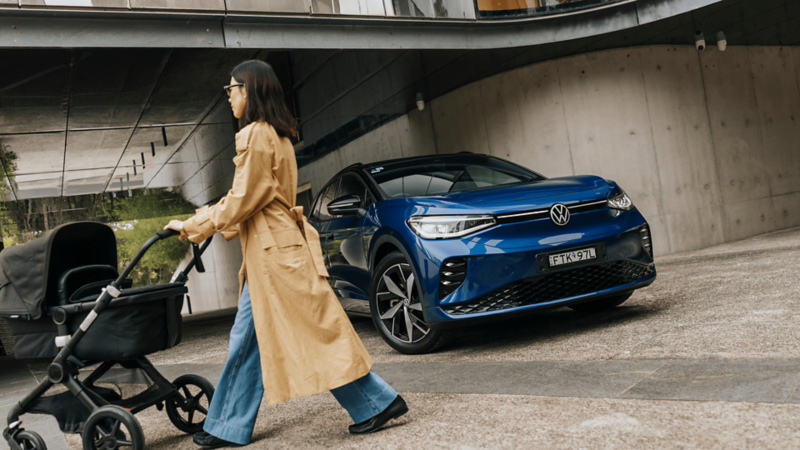 Woman pushing a pram next to a blue ID. 4 GTX