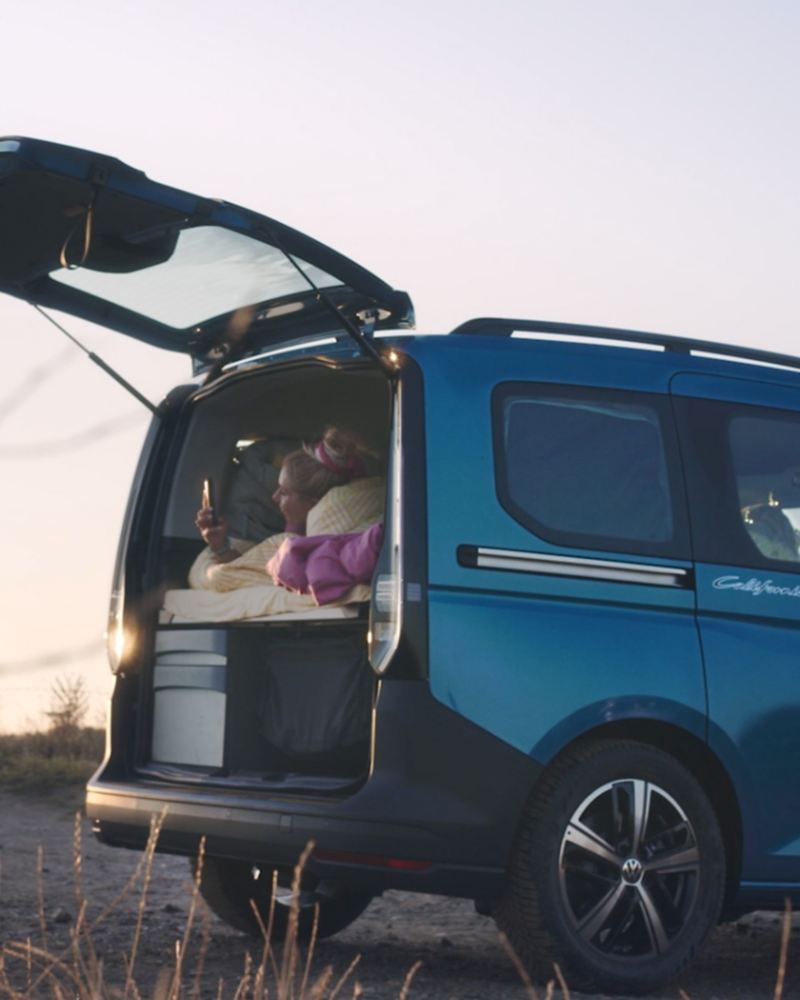 Person watching sunset out the rear door of Volkswagen Caddy California while lying in bed.