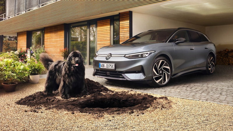VW ID.7 Tourer Pro unter Carport, davor ein schwarzer Hund, der Loch gebuddelt hat