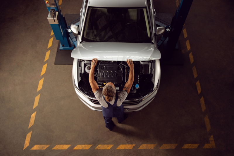 Mężczyzna w warsztatcie otwierający maskę białego Volkswagena