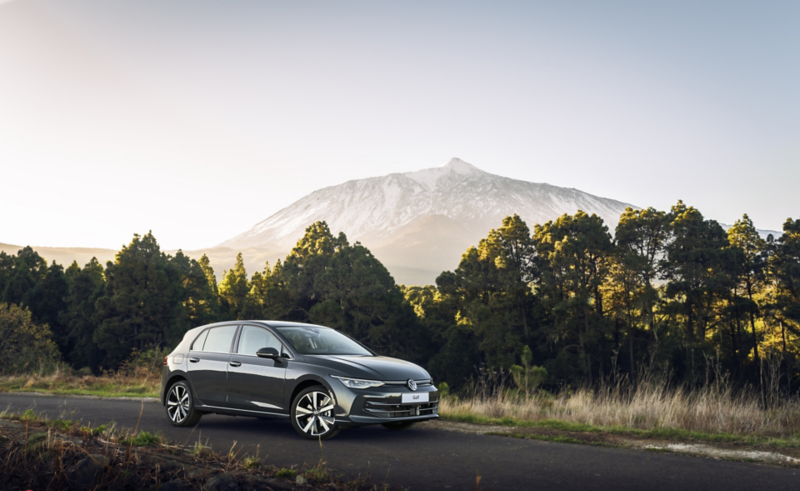 Volkswagen eHybrid blanco, vista lateral izquierda, al atardecer, aparcado en una carretera con luces festivas de fondo