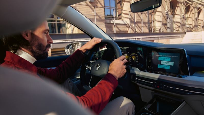 Mann sitzt in seinem Fahrzeug und nutzt die In-Car App Amazon Alexa