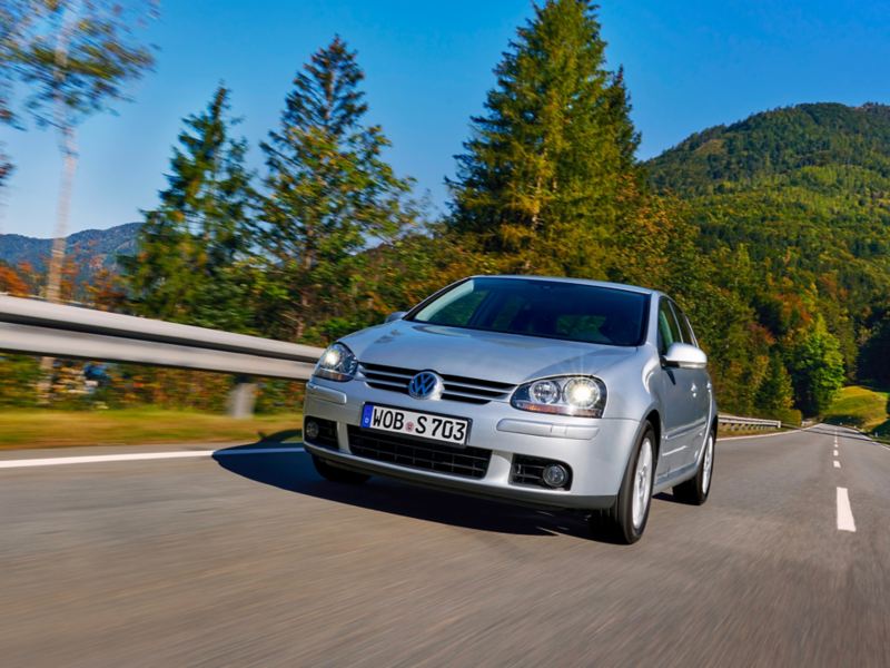 VW Golf 5 driving on a country road, green mountains in the background