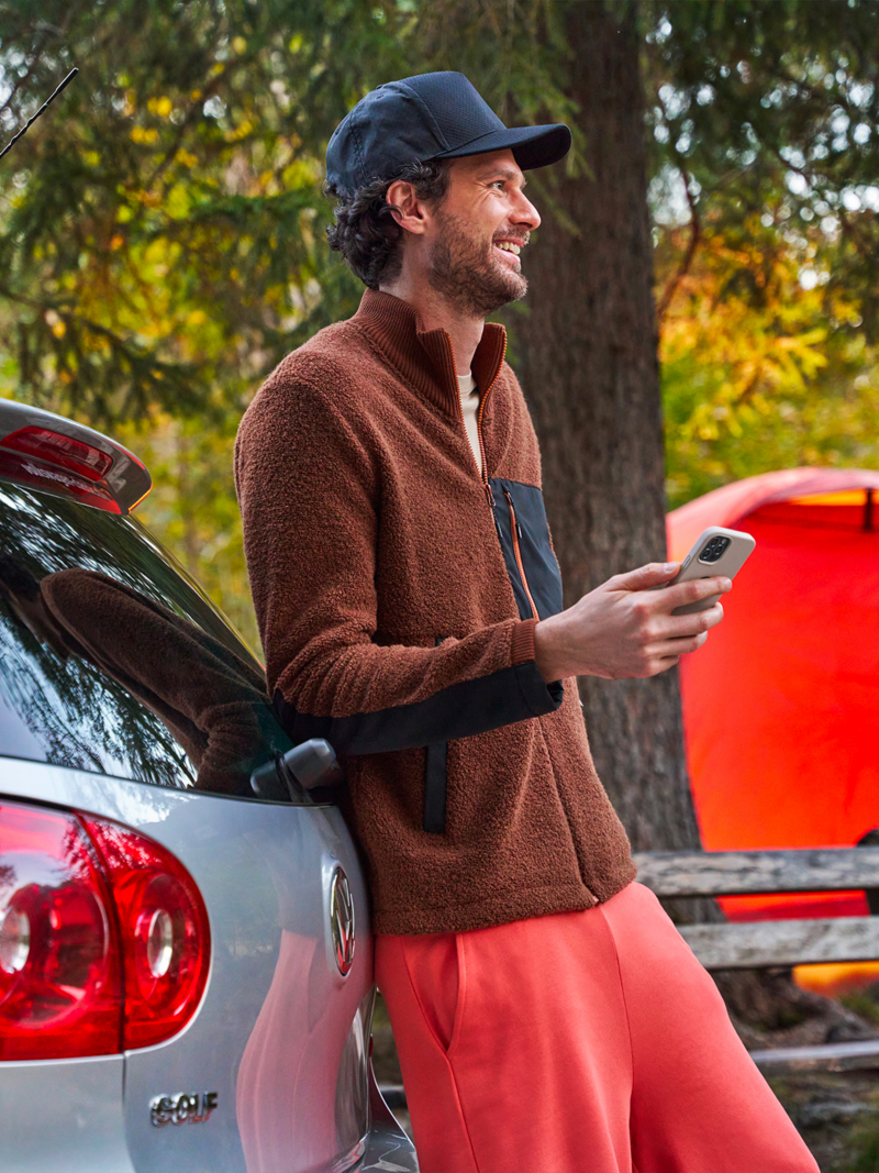 Man with smartphone in hand leaning against a VW Golf 5