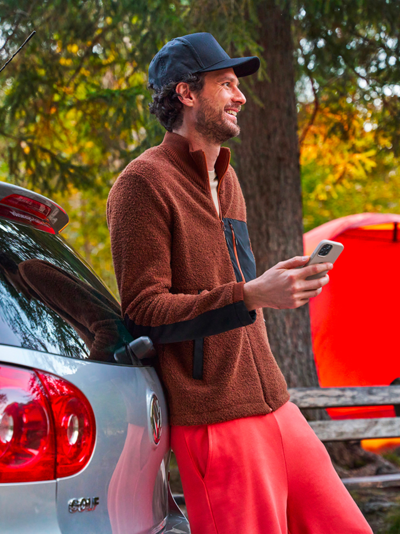 Un uomo con il suo smartphone in mano appoggiato al bagagliaio di una VW Golf 5.