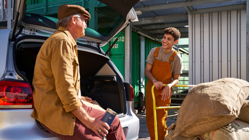 Two men are talking, one is sitting on the luggage compartment lid of a VW Golf 6