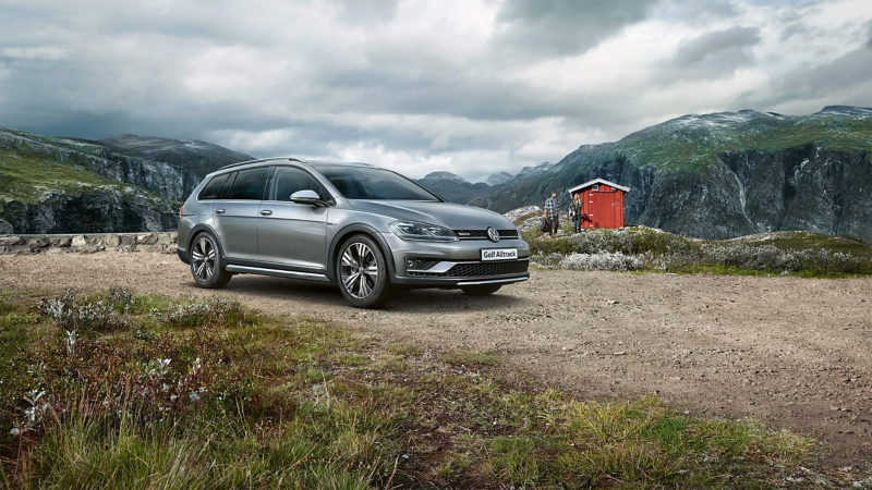 Golf All track parked in the mountains with couple hiking behind
