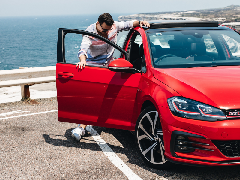 Man by the seaside entering his red Golf GTI