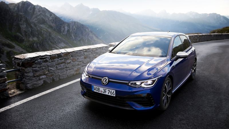 The new Golf R drives on the edge of a mountain road. Mountains are in the background.