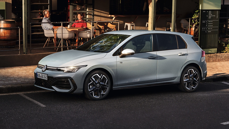 De Golf R-Line staat geparkeerd voor een wegrestaurant, met op de achtergrond een oudere man en een jonge vrouw.