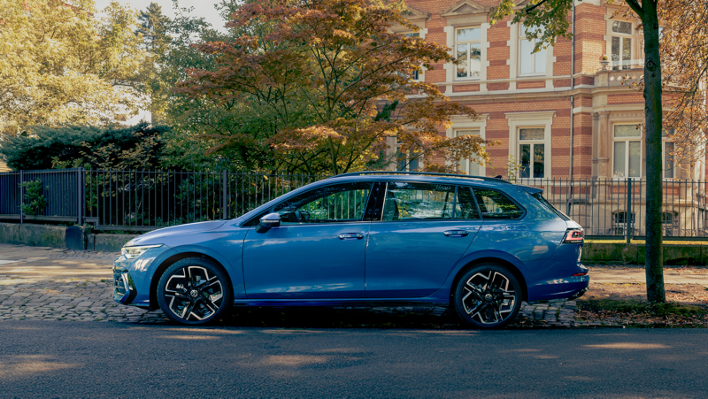 Zijaanzicht van de nieuwe Volkswagen Golf Variant R-Line in blauw, de auto staat geparkeerd in een straat met veel groen
