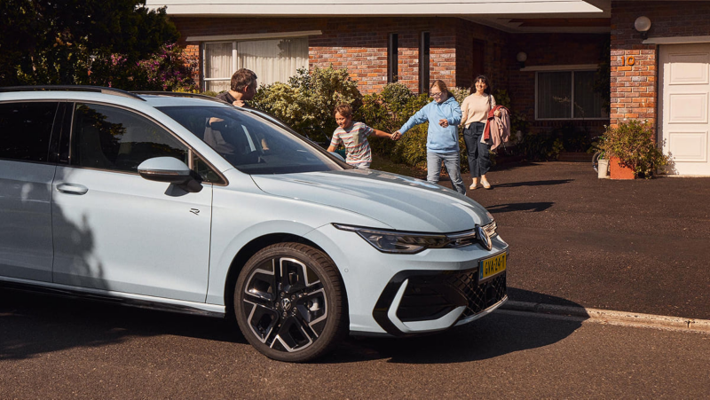 Een gezin loopt vanaf een woning naar de Volkswagen Golf Variant waar een vader uitstapt