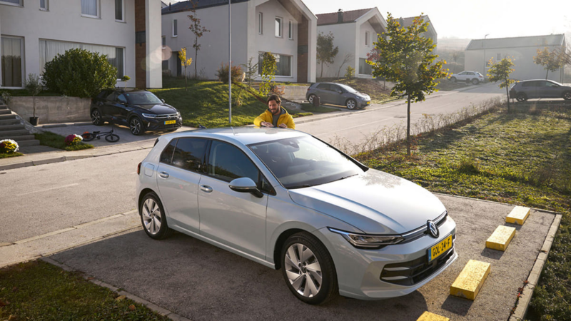 Man poetst zijn Volkswagen Golf die geparkeerd staat, hij staat aan de overkant van een weg naast een rij huizen
