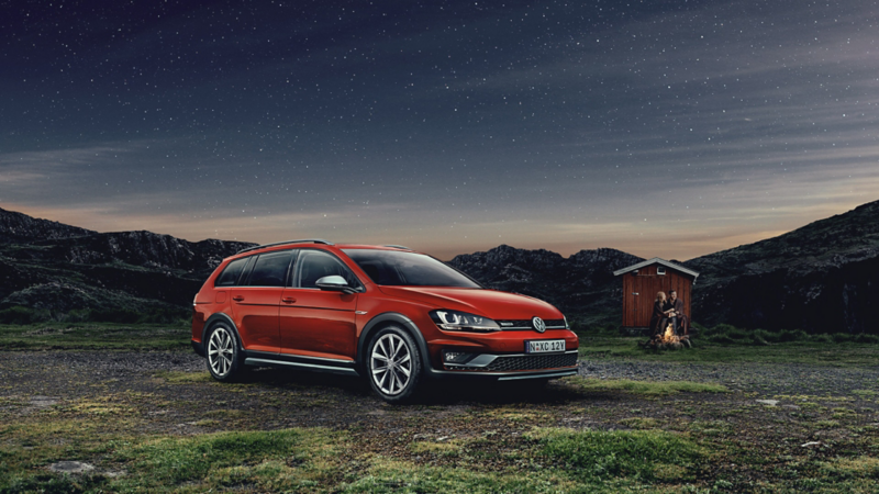 Golf Alltrack parked in a field with a man camping in the background at sunset