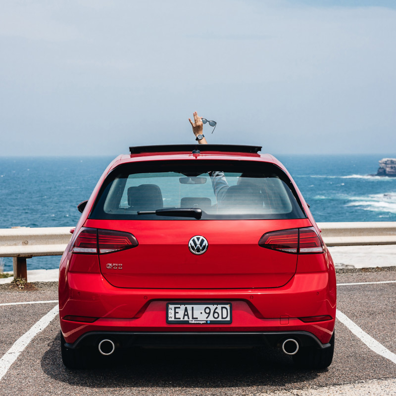 Man waving outside of his Golf GTI at the beach